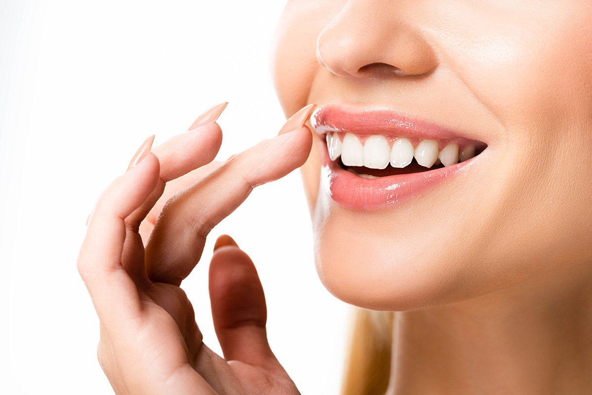 An image of a women touching her healthy white teeth.